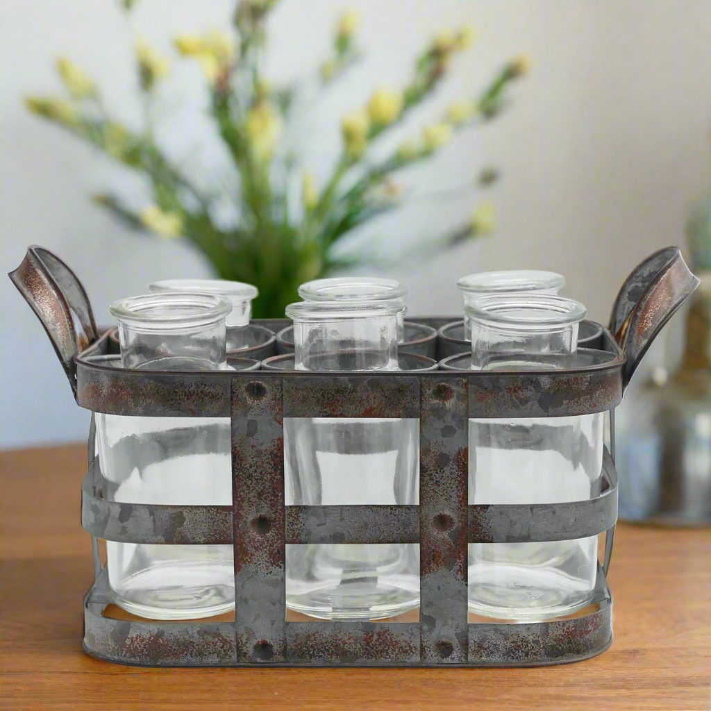 Metallic holder with six clear glass jars on a wooden surface with a blurred floral background