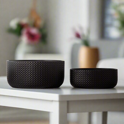 Two black textured bowls on a white table with a blurred background