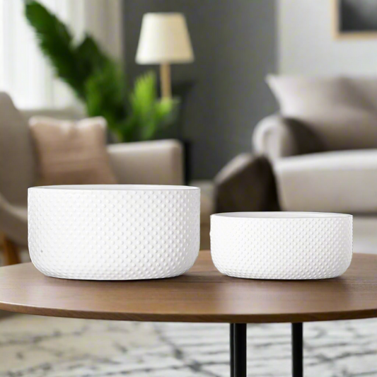 Two white ceramic planters with a geometric pattern, placed on a round table in a living room setting.