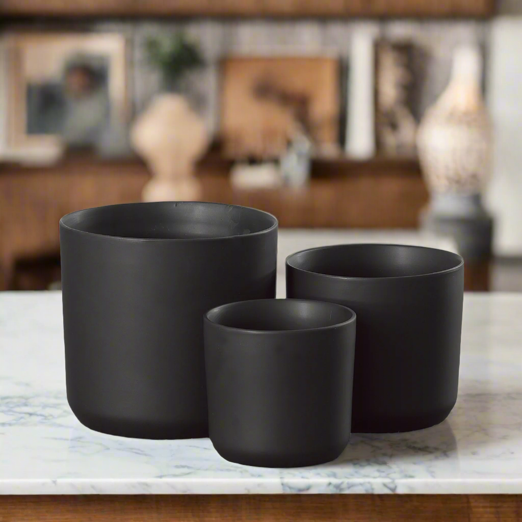 Three black plant pots on a marble surface with a blurred indoor setting in the background.