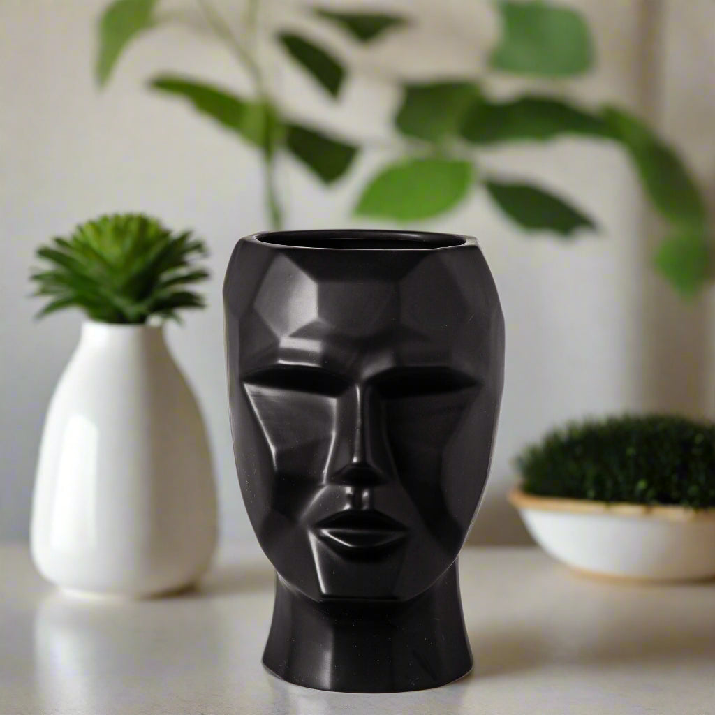Black vase shaped like a face on a white background