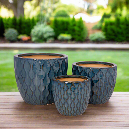 Three textured blue ceramic planters on a wooden surface with a garden background.
