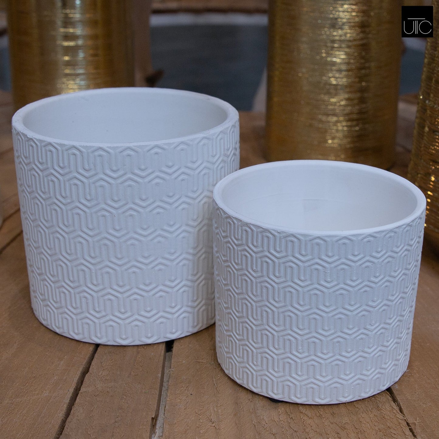 Two white ceramic cylindrical pots with embossed geometric lattice design on a wooden surface.