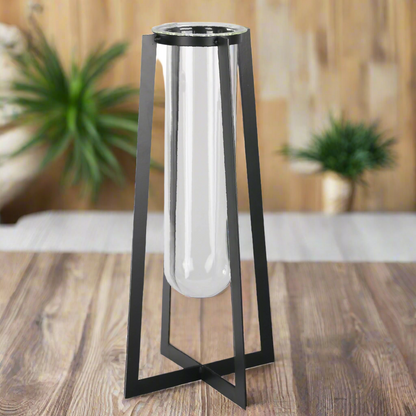 Black metal and glass cylindrical object on a wooden surface with plants in the background